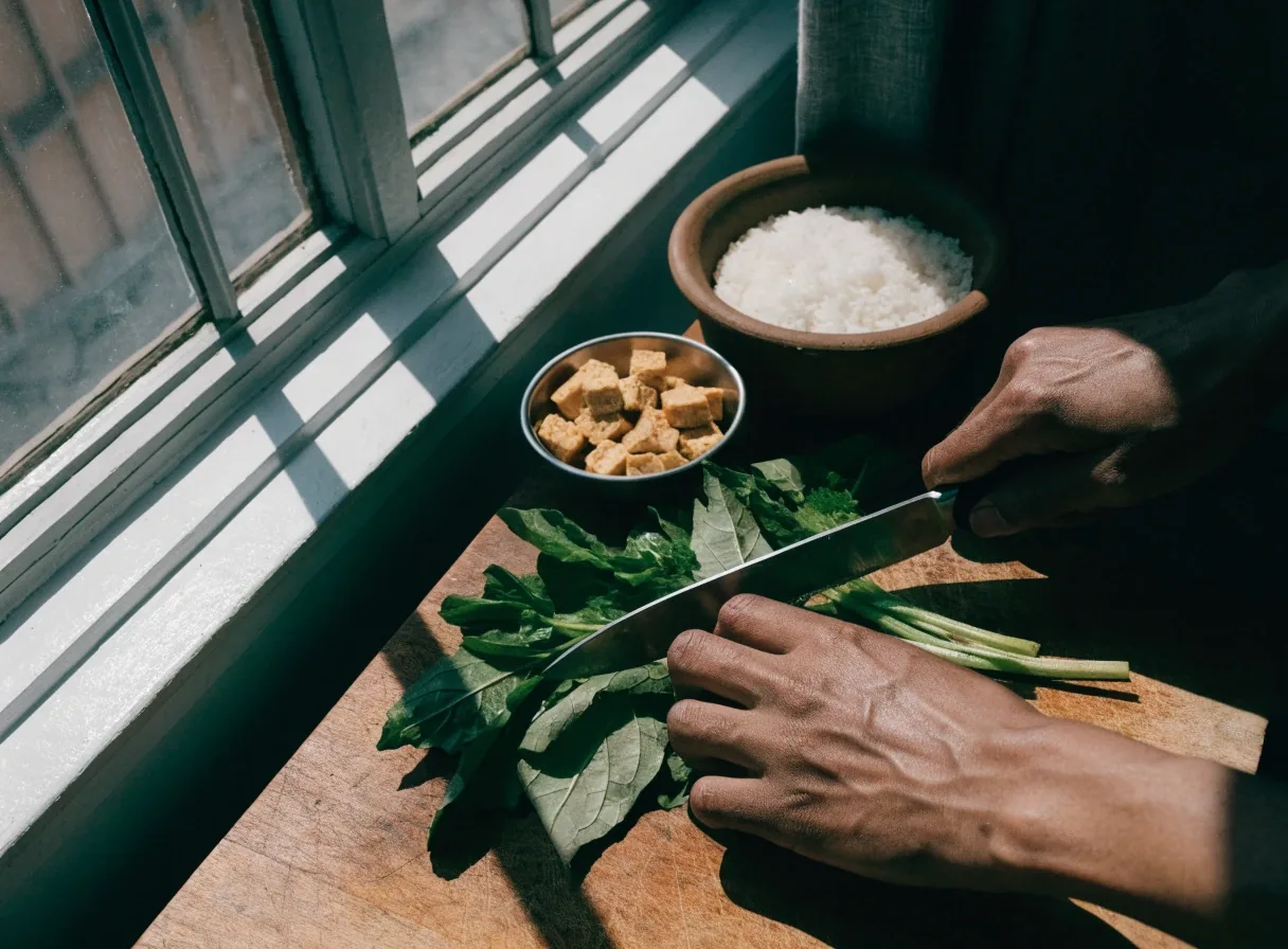 Two hands chopping greens on a wooden board with tempeh and rice nearby